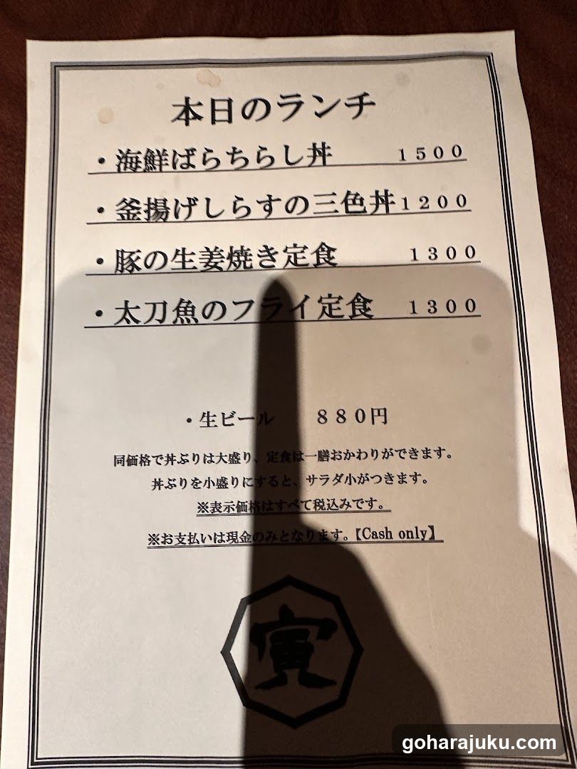 A printed menu listing lunch options with prices in yen, including seafood bowl, three-color rice dish, pork ginger-baked set meal, and swordfish fry set meal, along with beer price.