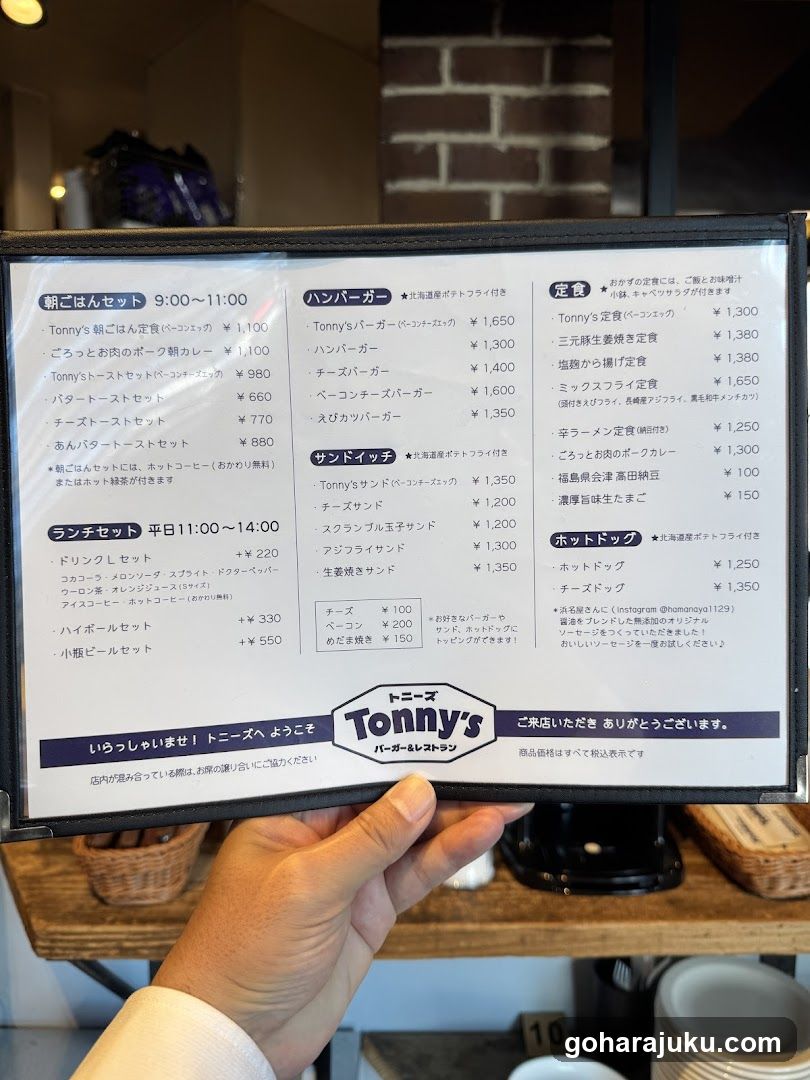 A close-up of a menu board held by hand, displaying various burger sets and prices in Japanese.