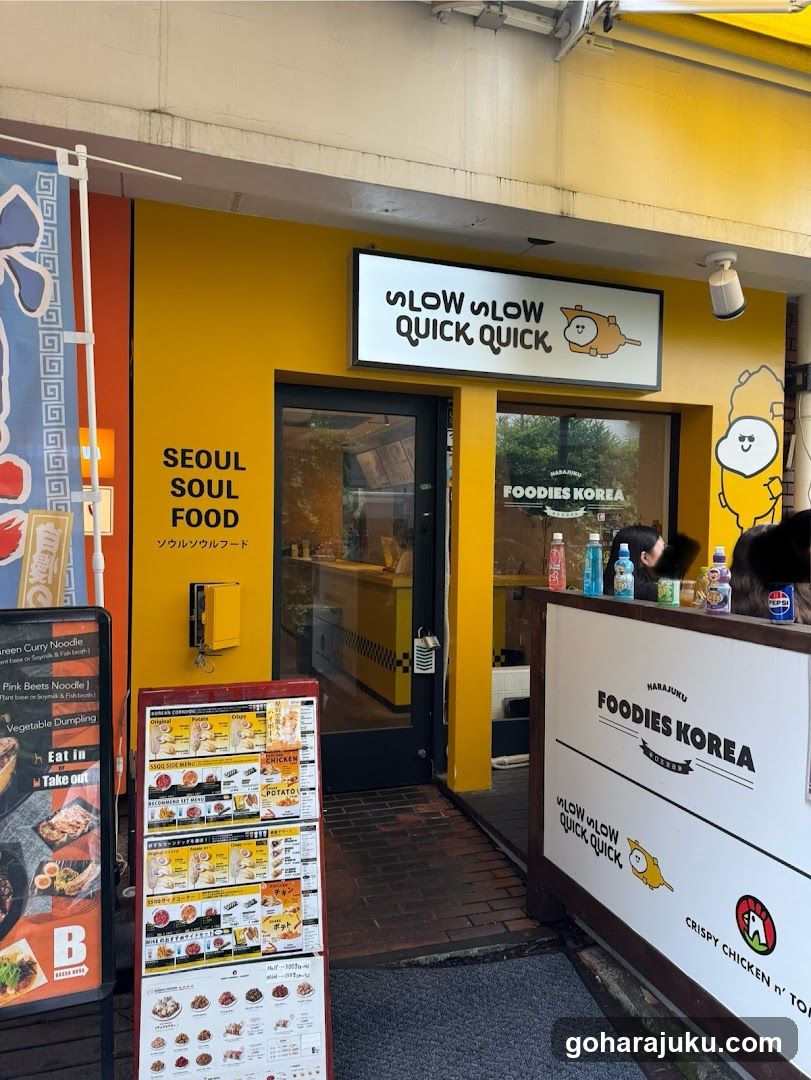 A bright yellow storefront with a sign reading 'SLOW SLOW QUICK QUICK' above the entrance. The wall features Korean text 'SEOUL SOUL FOOD'. A menu board stands outside, and a counter displays drinks and branding.