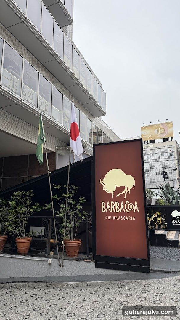 Photo of the physical exterior entrance and storefront facade of Barbacoa Churrascaria, featuring a large illuminated sign with a bull logo and Japanese flag visible nearby.