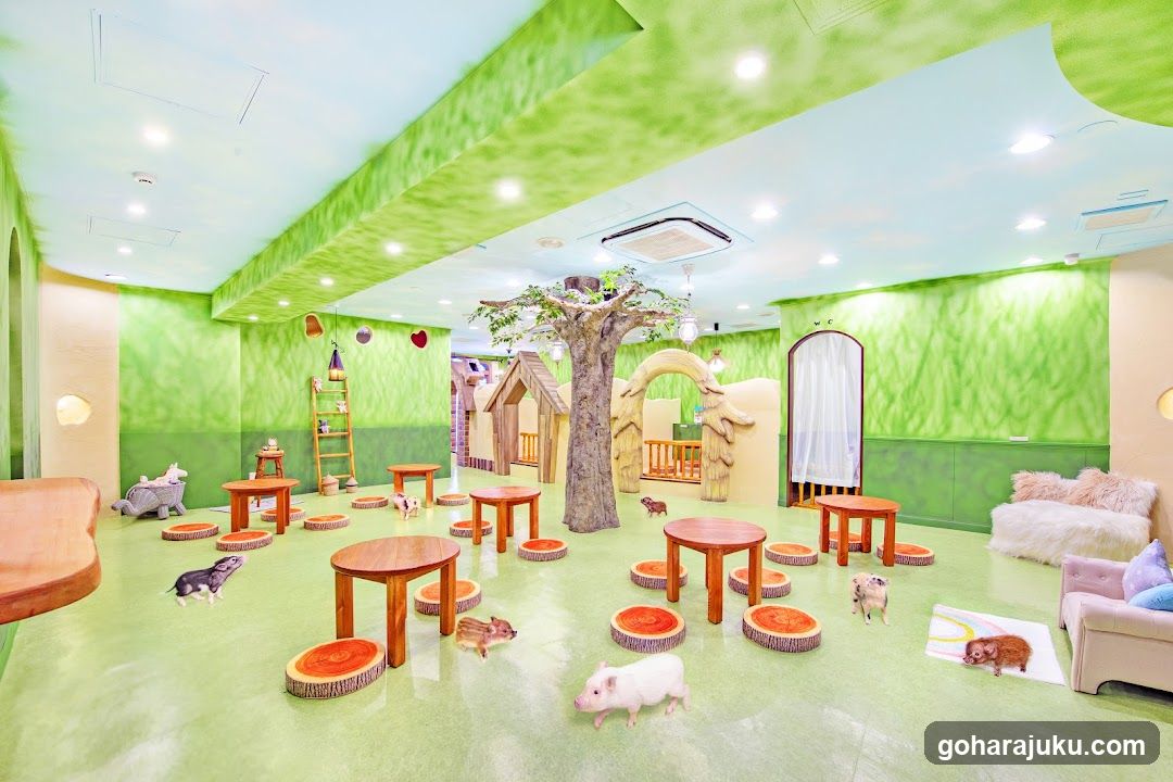 A brightly lit indoor space with green walls and ceiling, featuring animal figurines (pigs, hedgehogs) scattered on the floor. Wooden tables and stools are arranged throughout. Decorative elements include a tree trunk structure, wooden arches, and plush seating areas. No signage or menu visible.