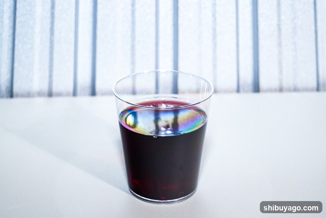 Glass of dark liquid with rainbow reflection