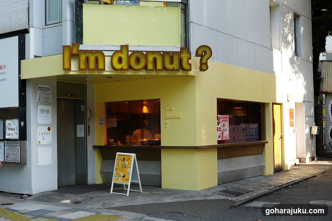 A yellow storefront with a large sign reading 'I'm donut ?' above the entrance. A sandwich board menu stands outside, and posters are visible on adjacent walls.