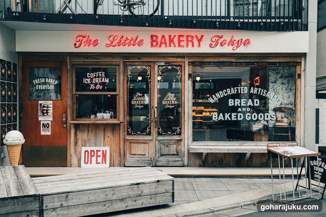 A charming bakery storefront with wooden doors and large windows displaying 'Handcrafted Artisan Bread and Baked Goods'. Signage includes 'Fresh Baked Everyday', 'Coffee Ice Cream To Go', and an open sign.