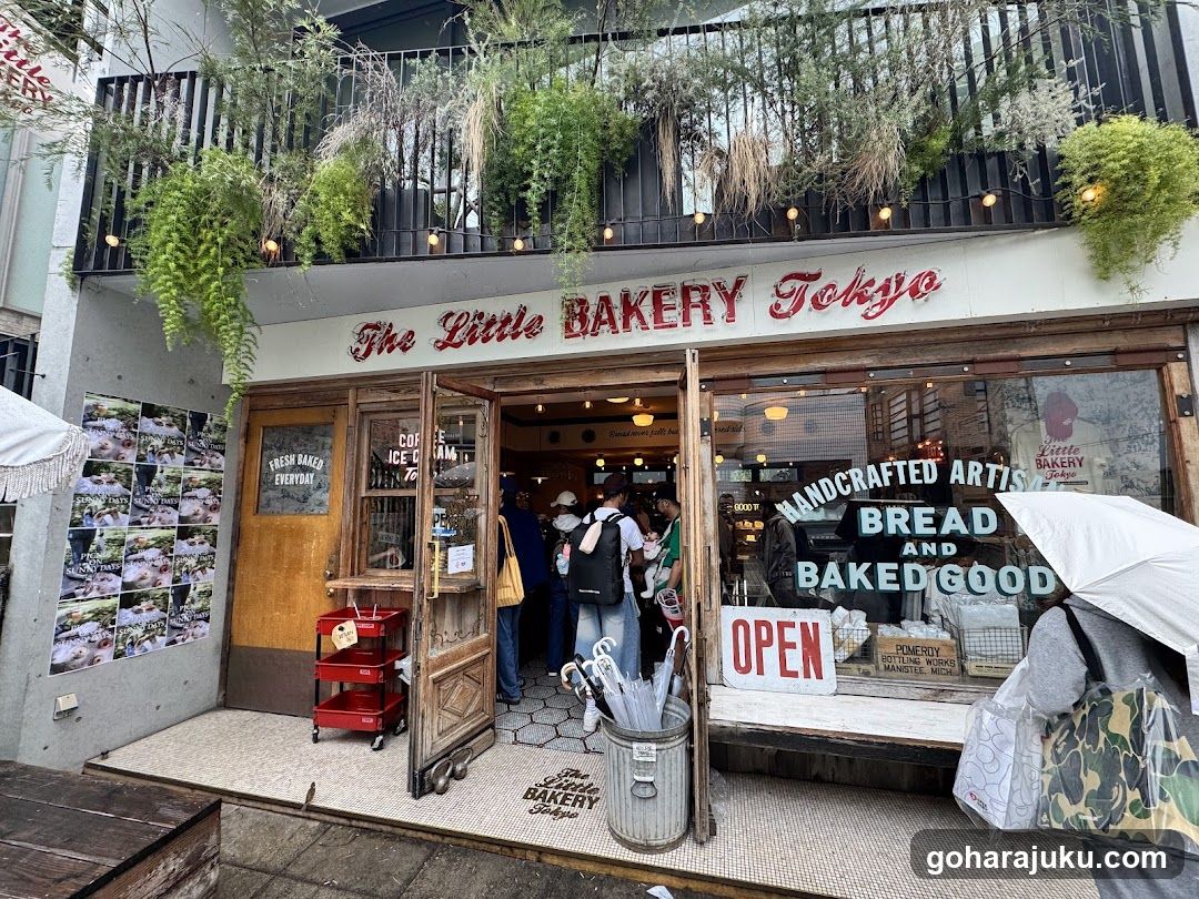 Exterior view of The Little Bakery Tokyo storefront with hanging plants, wooden doors, and signage reading 'Handcrafted Artisan Bread and Baked Good' on the window.