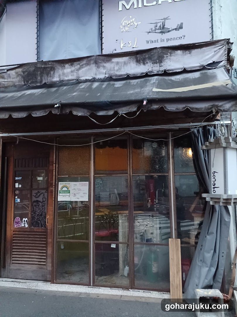 A shop front with a dark awning and large glass windows displaying interior furniture. A sign above reads 'KSL' with the phrase 'What is peace?' alongside an illustration of a helicopter.