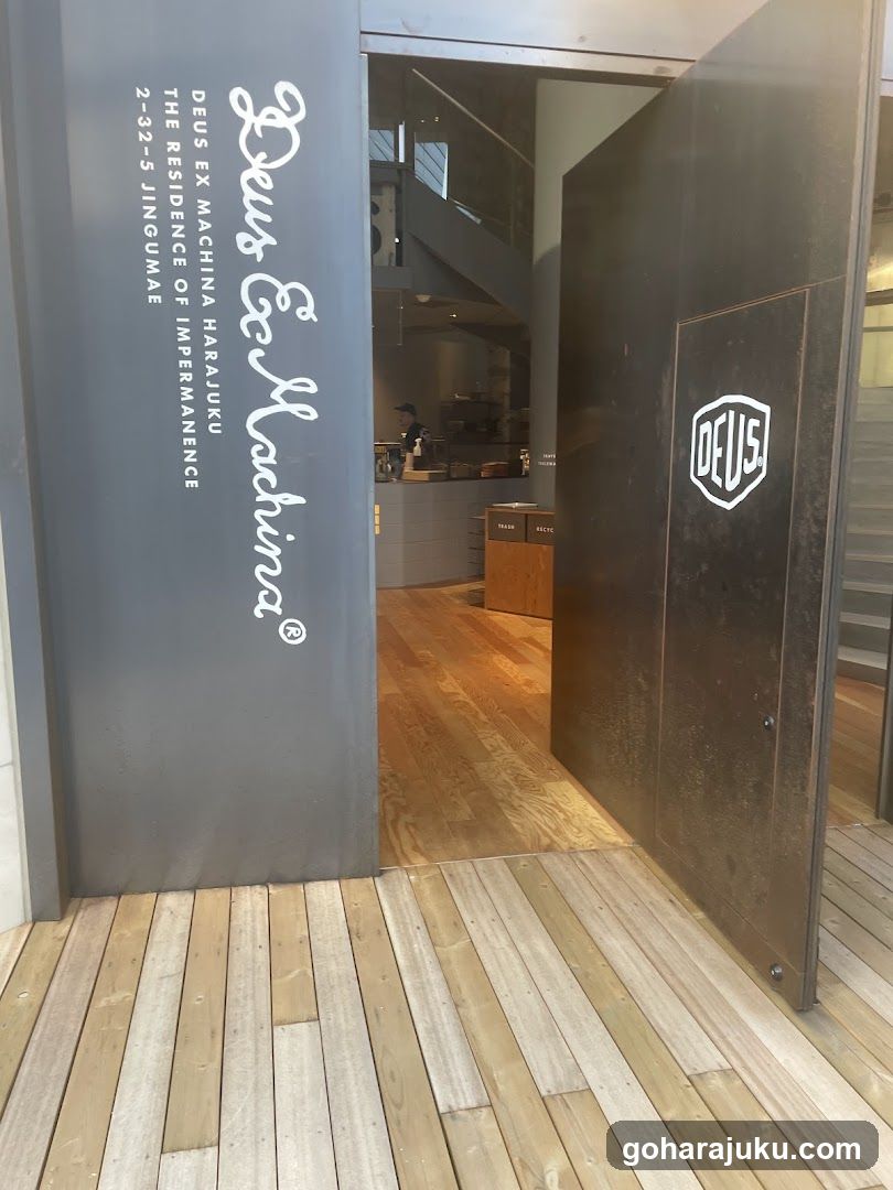 Photo of the physical exterior entrance to a shop named Deus Ex Machina, showing signage on the building facade with address details and interior view through open doors.