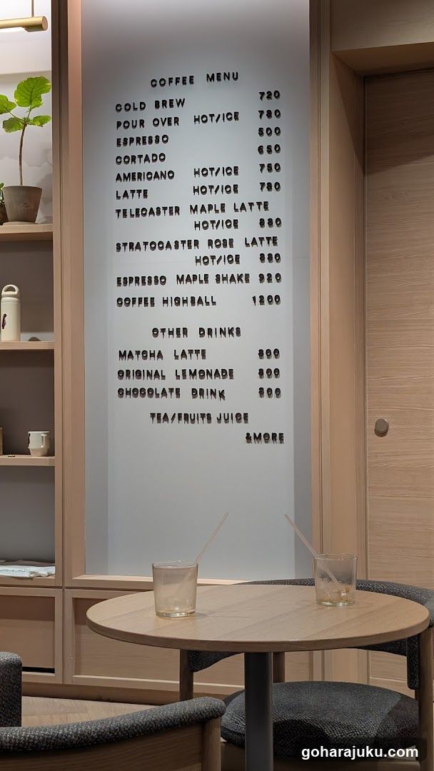 A frosted glass menu board mounted on a wooden wall, displaying coffee and other drink options with prices in KRW.