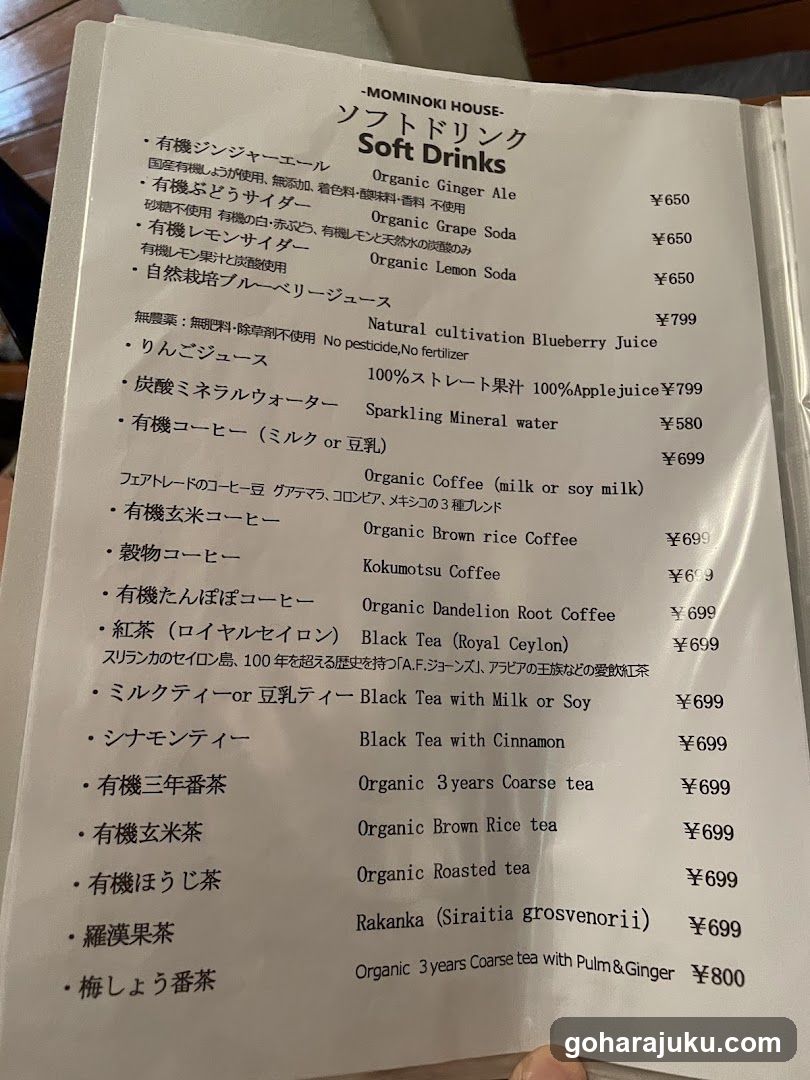 A close-up of a printed soft drinks menu from MOMINOKI HOUSE, featuring organic and natural cultivation beverages with prices in yen.