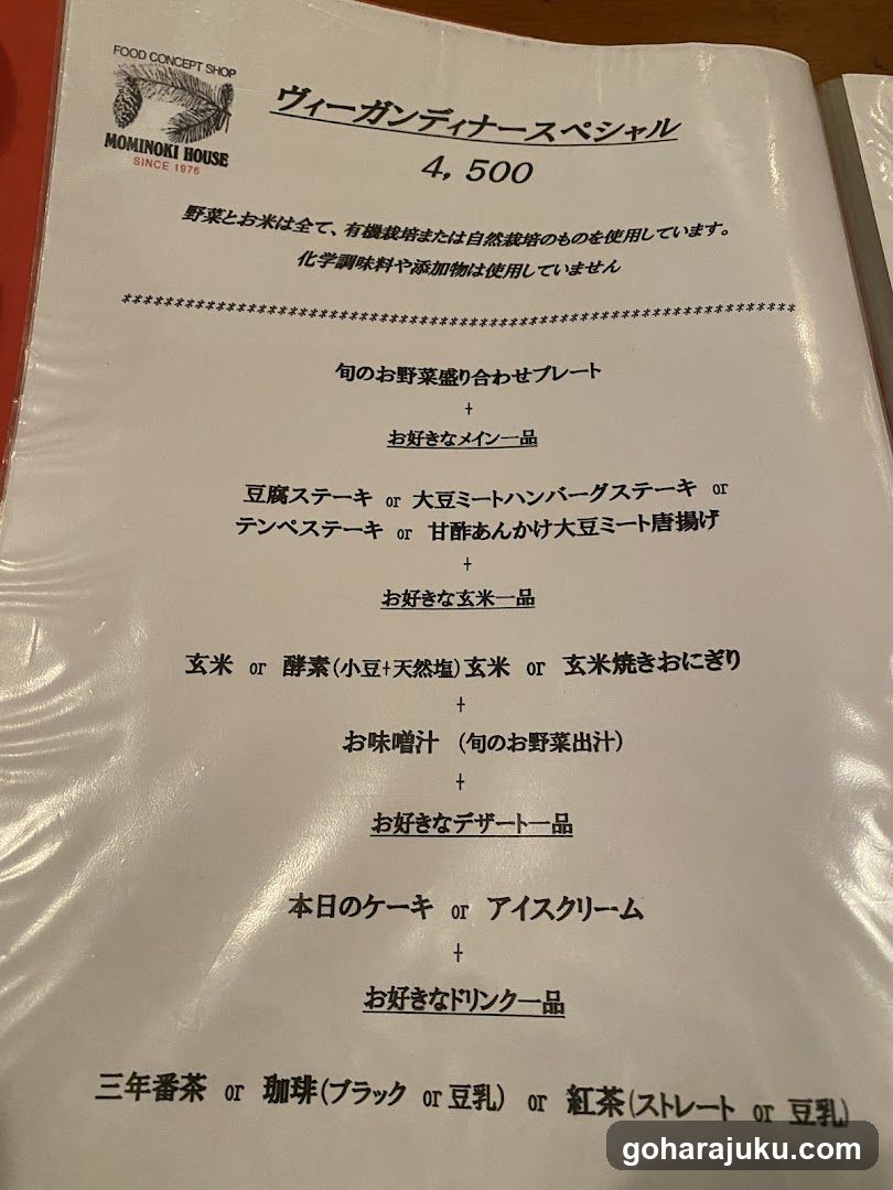 A printed menu from Nominoki House, featuring a vegan dinner special priced at 4,500 yen. The menu includes options like tofu steak, mushroom burger steak, and tempeh steak as main courses, with sides of rice or fermented soybean flour rice, soup, dessert (cake or ice cream), and drinks (green tea, matcha, milk tea, or red tea). It emphasizes organic ingredients and no chemical additives.