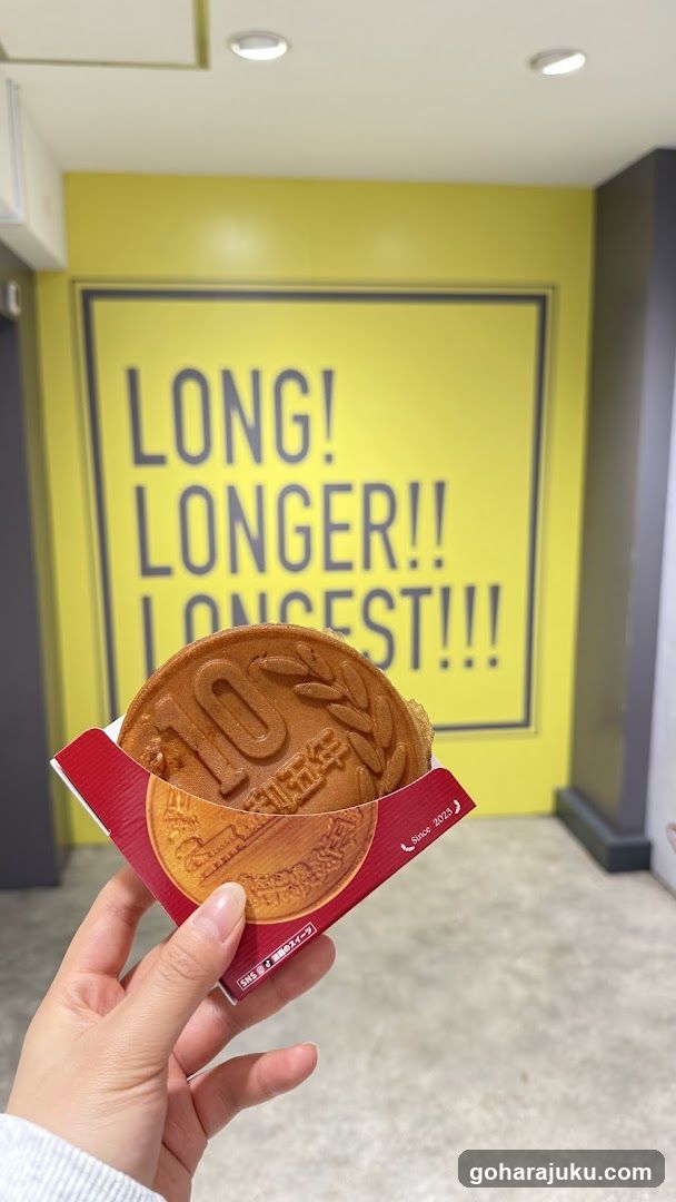 Hand holding a round cake with '10' embossed on it in front of a yellow wall with bold text.