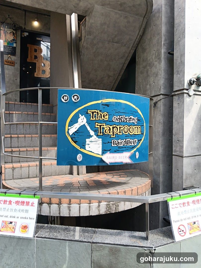 A photo of the exterior entrance to a bar or restaurant, featuring a blue sign with 'The Taproom' and 'Beer Bar' written on it. There is also a staircase leading up to the entrance.
